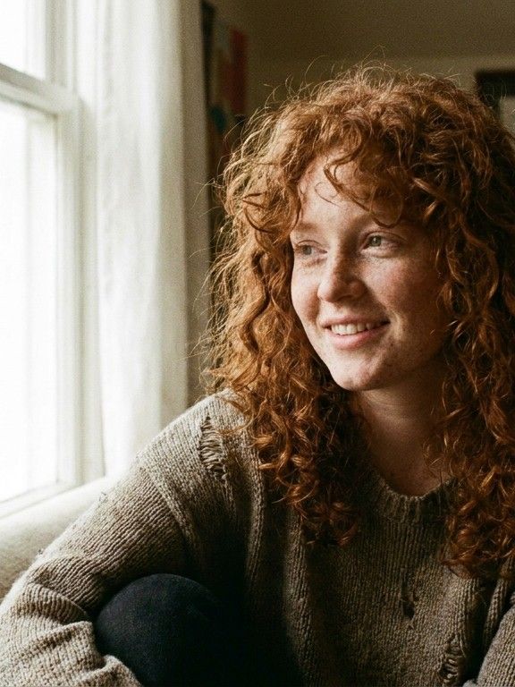Portrait of a young woman with freckles and curly red hair, natural window light, analog f
