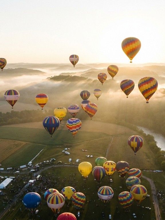 A hot air balloon festival at dawn with dozens of colorful balloons rising over misty hill